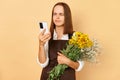 Puzzled confused woman florist holding bouquet of flowers calling to client to make order looking at phone display trying to find