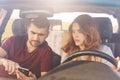 Puzzled couple sits in automobile, bearded man holds smart phone, uses online maps, tries to find way, being lost, have journey on