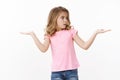 Puzzled cute young blond girl kid need make choice, raise hands sideways hold copyspace both arms, turn right looking at