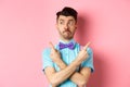 Puzzled funny man in bow-tie pointing fingers sideways, showing two variants on both sides, looking confused, standing