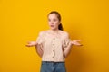 Puzzled girl, spreads hands with doubt,over yellow background. Teen girl faces dilemma, being unsure