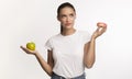 Puzzled Girl Standing Choosing Between Donut And Apple , White Background