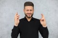 Puzzled handsome man with closed eyes is praying with fingers crossed isolated over gray background