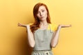 Puzzled hesitant girl with long red hair in gray apron and T-shirt