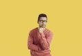 Puzzled male student in glasses isolated on yellow background thinking about something