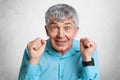 Puzzled mature handsome male looks with bewilderment and unexpectedness, clenches fists at camera, poses against white concrete wa Royalty Free Stock Photo