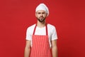 Puzzled perplexed young bearded male chef cook or baker man in striped apron white t-shirt toque chefs hat posing