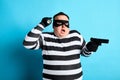 Puzzled plump thief holding a gun on a blue background