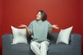 Puzzled pretty young girl dont know answer, spread hands, shrug shoulders, sitting on sofa on red studio background