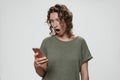 Puzzled stupefied curly hair woman opens eyes and mouth widely holding smartphone