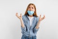 Puzzled, unsure young woman in a medical protective mask on her face, on a white background