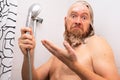 Puzzled wet soapy bearded man standing in bathtub holding shower in his hand and looking at the camera in bewilderment Royalty Free Stock Photo