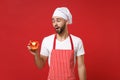 Puzzled young male chef cook or baker man in striped apron white t-shirt toque chefs hat isolated on red background