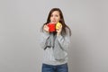 Puzzled young woman in gray sweater, scarf holding lemon, red cup of tea isolated on grey wall background. Healthy Royalty Free Stock Photo