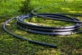 PVC water pipe is rolled up in large rings on green grass. Preparatory work for laying water pipes.