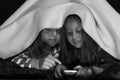 Pyjamas party for children: girls under blanket playing with phone