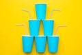 Pyramid Of Blue Paper Cups With Drinking Colored Plastic Straws On Yellow Background. Set For Party. Top View. Minimalist Style.