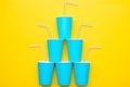 Pyramid Of Blue Paper Cups With Drinking Colored Plastic Straws On Yellow Background. Set For Party. Top View. Minimalist Style.