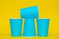 Pyramid of blue paper disposable cups on yellow background. Set for party. Copy, empty space for text Royalty Free Stock Photo