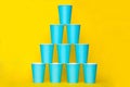 Pyramid of blue paper disposable cups on yellow background. Set for party. Copy, empty space for text Royalty Free Stock Photo