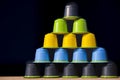 Pyramid of colorful compostable plastic coffee cups, black, blue, yellow and green, on a dark background with some copy space