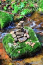 A pyramid of flat round stones stands on a large stone in the middle of a mountain rapid river