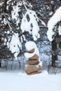 Pyramid from pebbles as tower in wintry forest under branches covered with snow