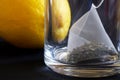 A pyramid tea bag with green tea in a transparent mug next to a fresh yellow lemon. Macro. Black style Royalty Free Stock Photo