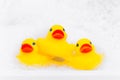 Pyramid of three yellow rubber duck for bathing in the bathroom among relaxing bubble baths, front view, copy space for