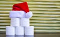 A pyramid of toilet paper with a Santa Claus hat against a gold background