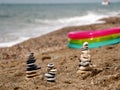 Pyramids of small flat stones stand on the sandy seashore. Behind the pyramids on the sand is an inflatable baby bath.