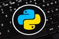 Python programming language round logo sticker, symbol label laying on a laptop keyboard, closeup, top view. Simple programming