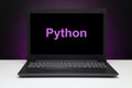 Python text on laptop screen on textured black background with purple light.