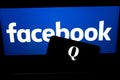 QAnon vs FACEBOOK. QAnon organisation logo seen on the smartphone which is placed on Facebook logo