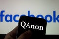 QAnon vs FACEBOOK. QAnon organisation logo seen on the smartphone which is placed on Facebook logos.