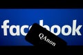 QAnon vs FACEBOOK. QAnon organisation logo seen on the smartphone which is placed on Facebook logos.