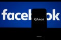 QAnon vs FACEBOOK. QAnon organisation logo seen on the smartphone which is placed on Facebook logos.