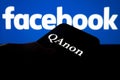 QAnon vs FACEBOOK. QAnon organisation logo seen on the smartphone which is placed on Facebook logos.