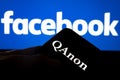 QAnon vs FACEBOOK. QAnon organization logo seen on the smartphone which is placed on Facebook logo.