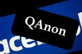 QAnon vs FACEBOOK. QAnon organisation logo seen on the smartphone which is placed on Facebook logos.