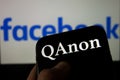 QAnon vs FACEBOOK. QAnon organization logo seen on the smartphone which is placed on Facebook logos.