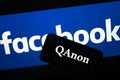 QAnon vs FACEBOOK. QAnon organization logo seen on the smartphone which is placed on Facebook logos.