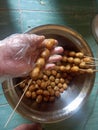 Quail egg skewers in the hand of an Asian man, and a pile of eggs with a sweet and savory taste in a stainless container