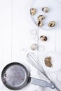 Quail eggs in a plate, a shell, a whisk for beating and a frying pan on a white wooden background. view from above Royalty Free Stock Photo