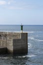 A quaint green lighthouse stands on a stone pier, overlooking tranquil blue waters beneath a partly cloudy sky