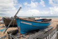 A quaint small blue wooden rowing boat berthed on wooden beams on a pebble beach next to another wood boat. Royalty Free Stock Photo