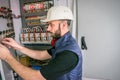 A qualified engineer works in an electrical panel. Worker repairs high-voltage equipment. An electrician in a helmet connects the