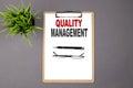 QUALITY MANAGEMENT on the brown clipboard on the grey background. Business concept Royalty Free Stock Photo