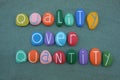 Quality over quantity, conceptual phrase composed with multi colored stone letters over green sand Royalty Free Stock Photo