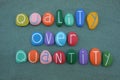 Quality over quantity, conceptual phrase composed with multi colored stone letters over green sand